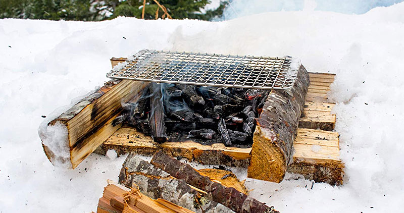 Campfire in the snow, with hot coals and a cooking grill
