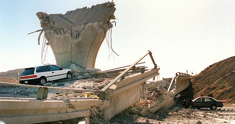 A collapsed highway overpass from an earthquake with cars trapped in the rubble
