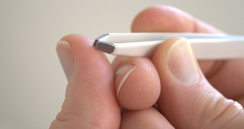 Tweezers pulling something from a thumb