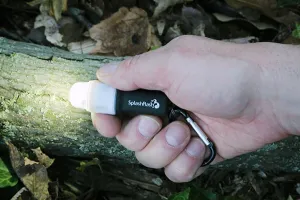 Ultimate Survival Technologies SplashFlash LED Light in a hand above a branch