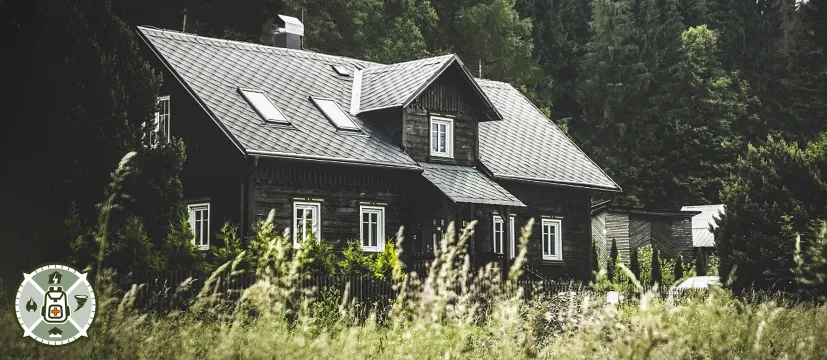 A home in the woods behind a field of grass