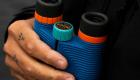 Nocs Provisions Standard Issue binoculars held outdoors while scanning a hazy horizon for wildfire smoke and grid emergencies